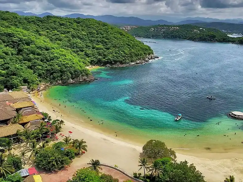 Vista aérea de una bahía de Huatulco con agua turquesa, arena clara y selva en los cerros