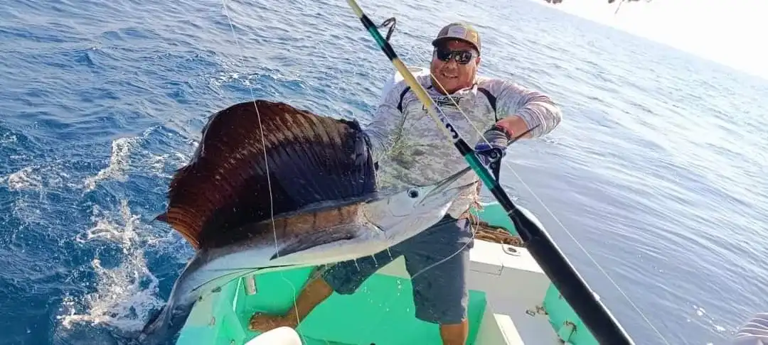Pescador con caña a bordo de una lancha junto a un pez vela recién sacado del mar